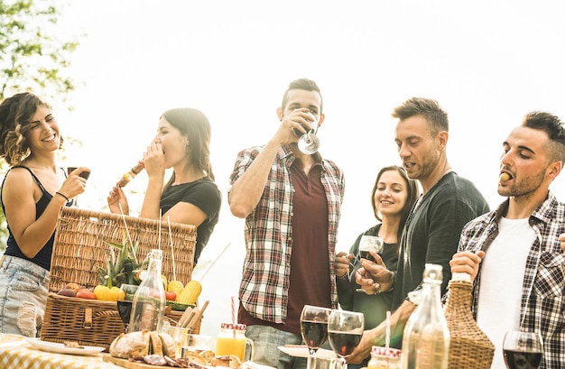 Young friends having fun outdoors drinking red wine and talking at barbecue party