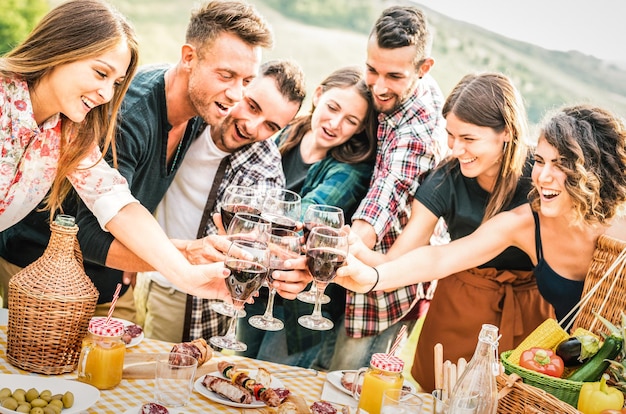 Young friends having genuine fun outdoor toasting red wine at open air barbq party