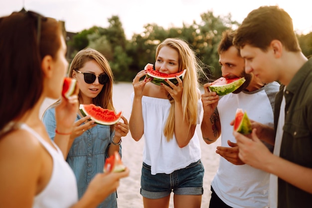 Photo young friends relaxing on the beach and eating watermelon people summer lifestyle