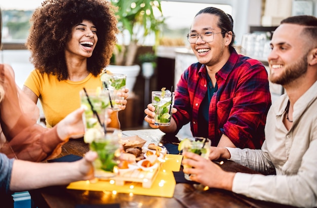 Young friends toasting mojito drinks at fashion cocktail pub restaurant