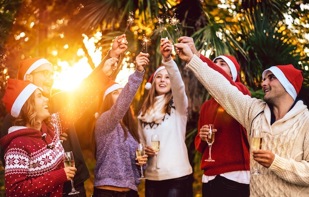 Young friends with santa hats celebrating Christmas with champagne wine toast outdoors