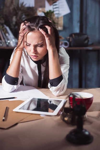 Young frustrated woman working at loft home or office desk in front of laptop suffering from chronic daily headaches