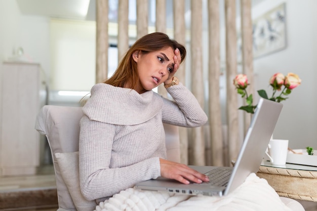 Young frustrated woman working at office desk in front of laptop suffering from chronic daily headaches, treatment online, appointing to a medical consultation, electromagnetic radiation, sick pay