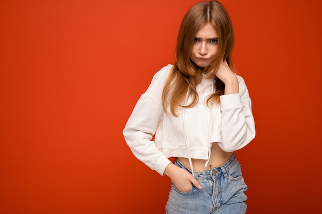 Young funny beautiful dark blonde female person with sincere emotions isolated on background with copy space wearing casual white hoodie. Emotional concept.