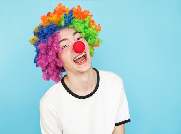 Young funny male teenager in white t-shirt on blue background in clown wig