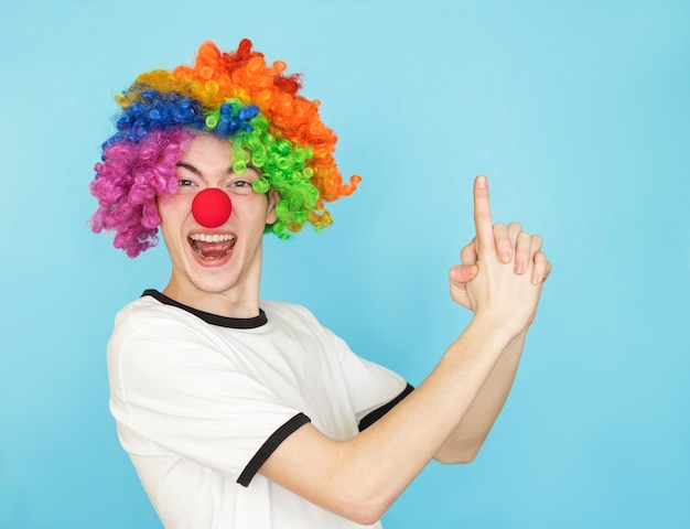 Young funny male teenager in white t-shirt on blue background in clown wig