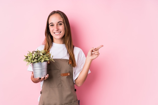 Young gardener caucasian woman isolated smiling and pointing aside, showing something at blank space.