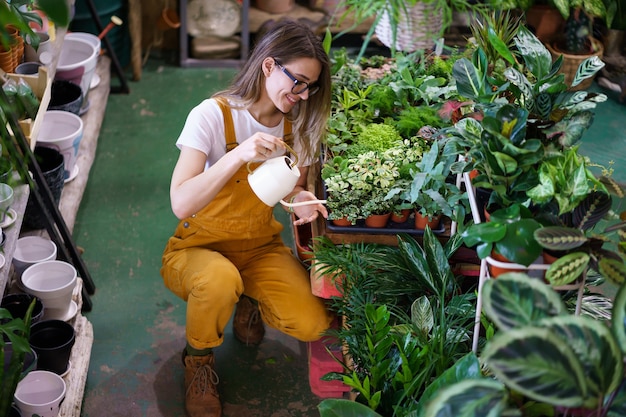 Young gardener girl work in glasshouse water potted houseplants female florist care of house plants