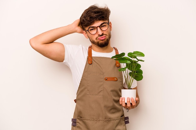 Young gardener hispanic man holding a plant isolated on white background being shocked she has remembered important meeting