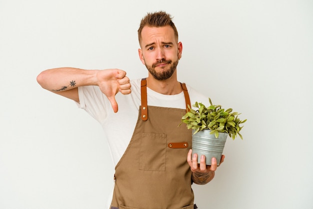 Young gardener tattooed caucasian man holding a plant isolated on white background showing a dislike gesture, thumbs down. Disagreement concept.