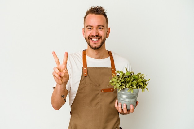 Young gardener tattooed caucasian man holding a plant isolated on white background showing number two with fingers.