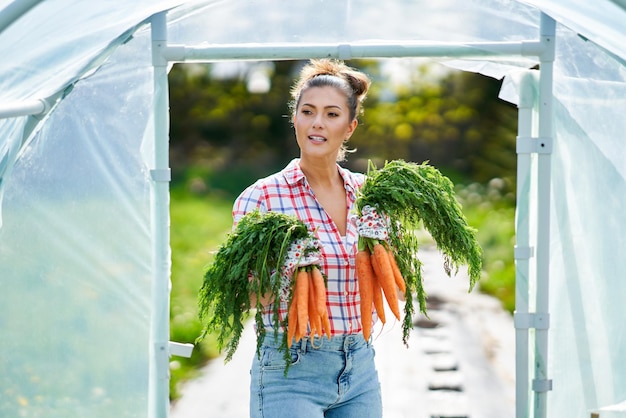 Young gardener woman with carrots in greenhouse