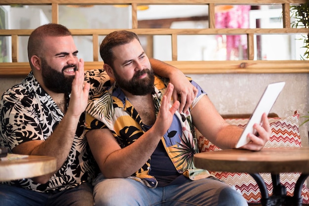 Young gay couple having a remote conversation with other people via video call from their tablet