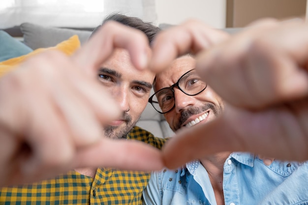 Young gay couple smiling confident doing heart symbol with hands at home