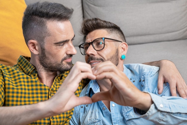 Young gay couple smiling confident doing heart symbol with hands at home