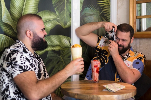 Young gay couple taking pictures while drinking a cocktail in a tropical bar Tourism summer and travel concept