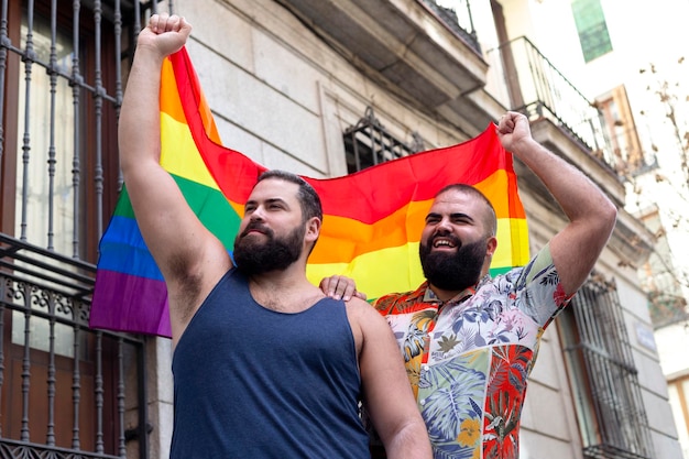 Young gay couple waving rainbow flag together on the street LGBT pride concept