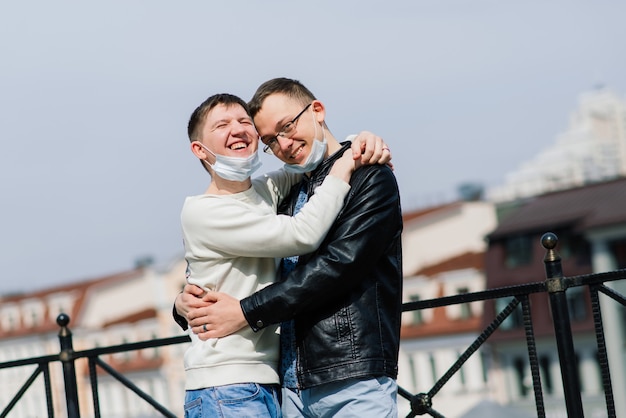 Young gay couple wearing medical mask hugging at the city.