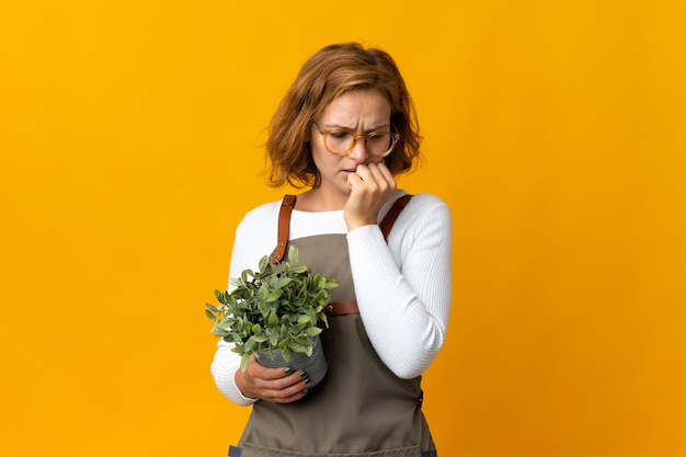 Young Georgian woman holding a plant isolated on yellow background having doubts