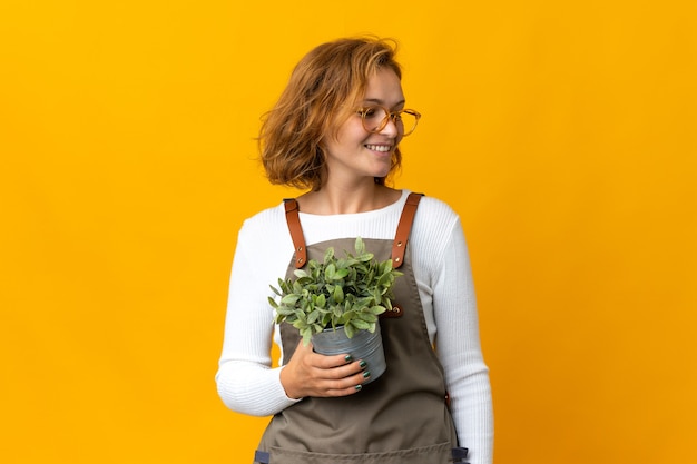 Young Georgian woman holding a plant isolated on yellow background looking side