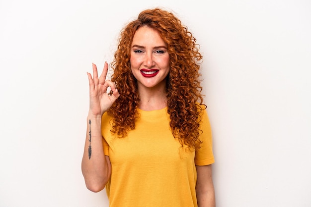 Young ginger caucasian woman isolated on white background cheerful and confident showing ok gesture