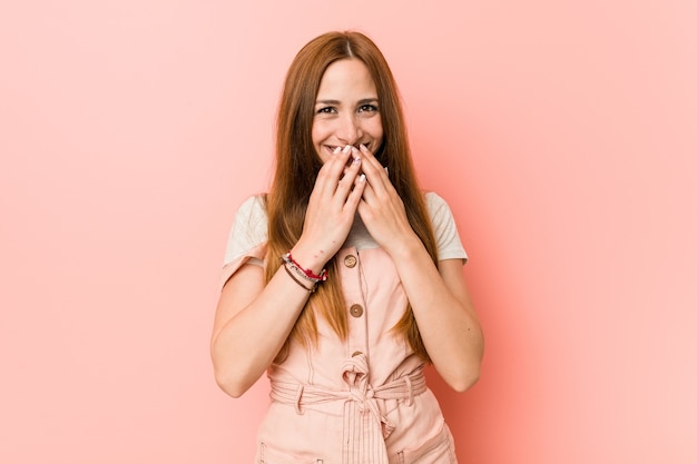 Young ginger woman with freckles laughing about something, coning mouth with hands.