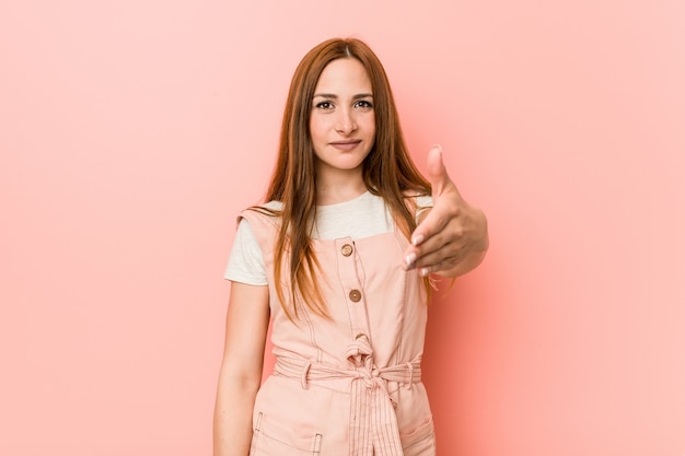 Young ginger woman with freckles stretching hand at camera in greeting gesture.