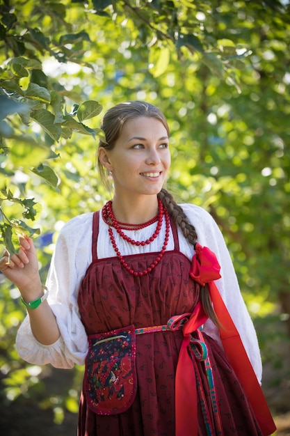 A young girl of amazing beauty stands under the branches of a tree on a green background, close up