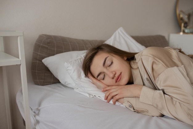 A young girl in beige pajamas sleeps on a white bed.