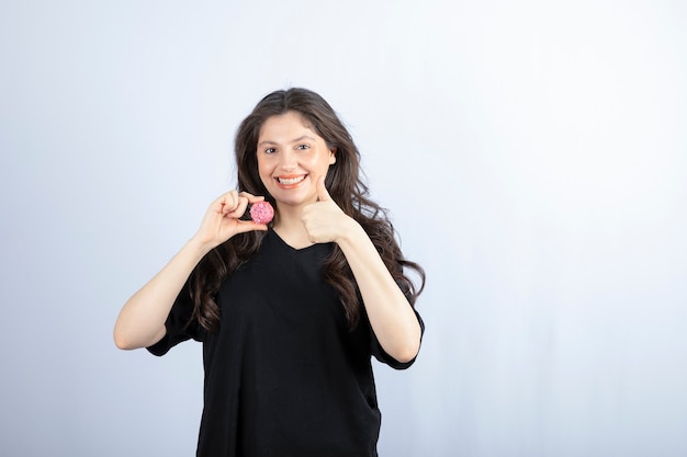 Young girl in black outfit holding pink cookie and showing thumb up. 