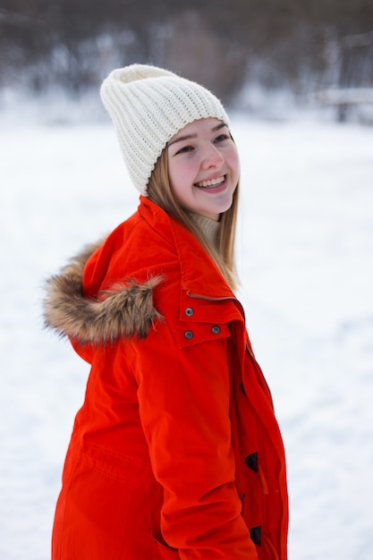 A young girl, blonde, in a sweater, a hat and an orange jacket, against the backdrop of the winter landscape. Snow and frost, the concept of Christmas.