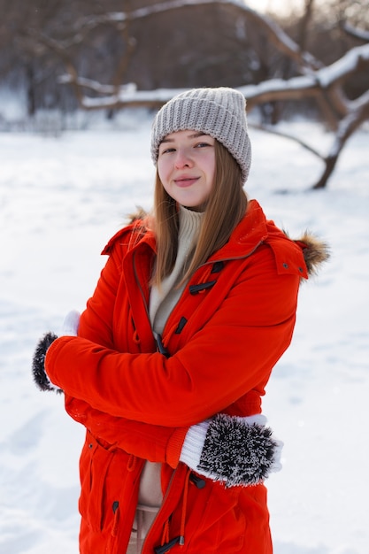 A young girl, blonde, in a sweater, a hat and an orange jacket, against the backdrop of the winter landscape. Snow and frost, the concept of Christmas.