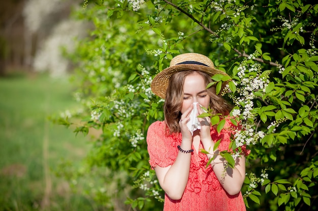 Young girl blowing nose and sneezing in tissue in front of blooming tree