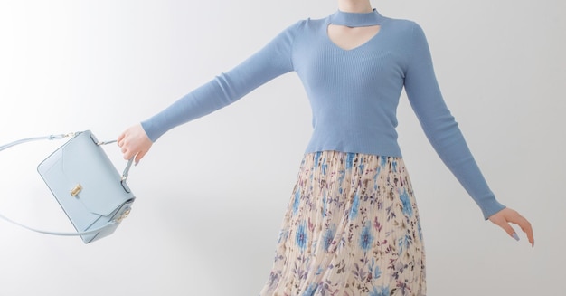 Young girl in blue blouse and pleated skirt with blue handbag on white background