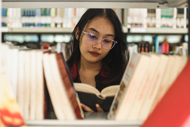 Young girl behind book shelves picking and choosing a book in library