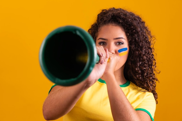 Young girl brazilian cheerleader with a vuvuzela on yellow background celebrating