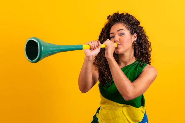 Young girl brazilian cheerleader with a vuvuzela on yellow background celebrating