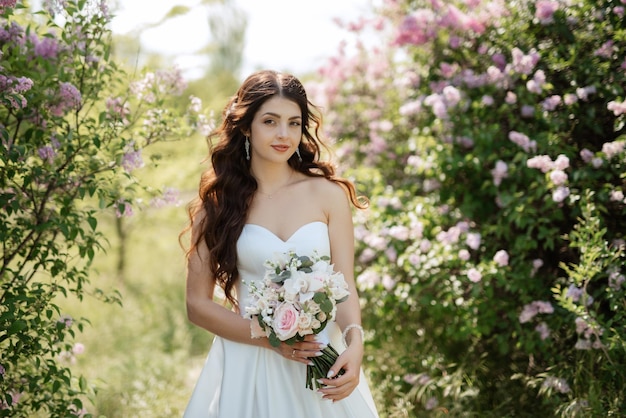 Young girl bride in a white dress in a spring forest in lilac bushes