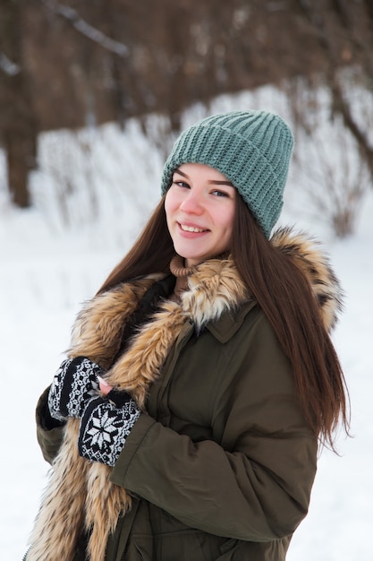 A young girl, brunette, in sweater, a hat and an green jacket, against the backdrop of the winter landscape. Snow and frost, the concept of Christmas.