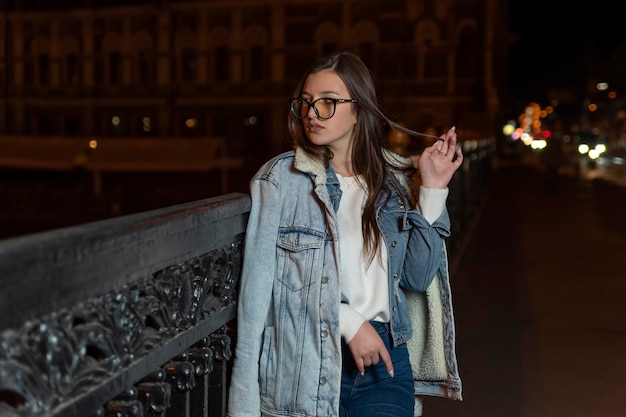 Young girl in casual style on evening city background Stylish girl walk on night city street