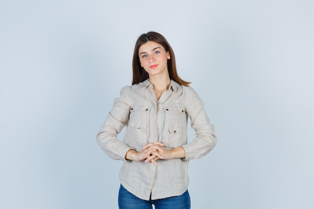 Young girl clasping hands in beige shirt, jeans and looking cute. front view.