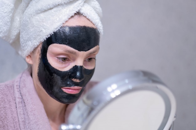 Young girl in a cleansing black coal mask on her face. 