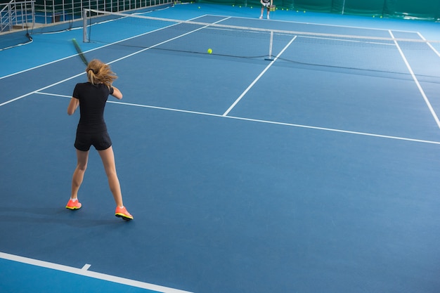 The young girl in a closed tennis court with ball and racket