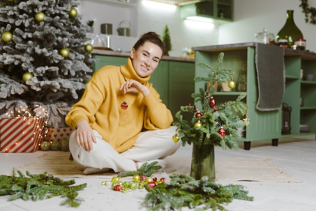 A young girl collects Christmas decor from fir branches in the kitchen the concept of Christmas