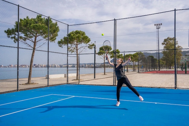 Young girl in a dark blue dress plays tennis on the court with a hard coating of blue