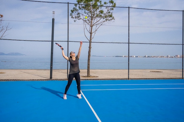 Young girl in a dark blue dress plays tennis on the court with a hard coating of blue