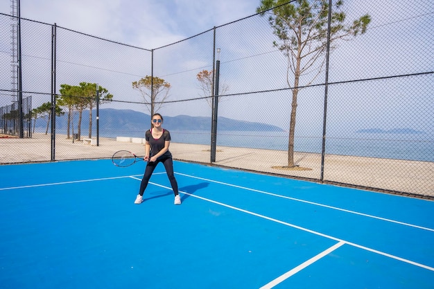 Young girl in a dark blue dress plays tennis on the court with a hard coating of blue