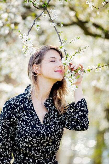 Young girl in dark dress stay near a flowering tree in the park. Spring season