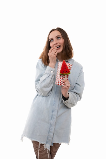 A young girl in a denim shirt holds a lollipop and popcorn