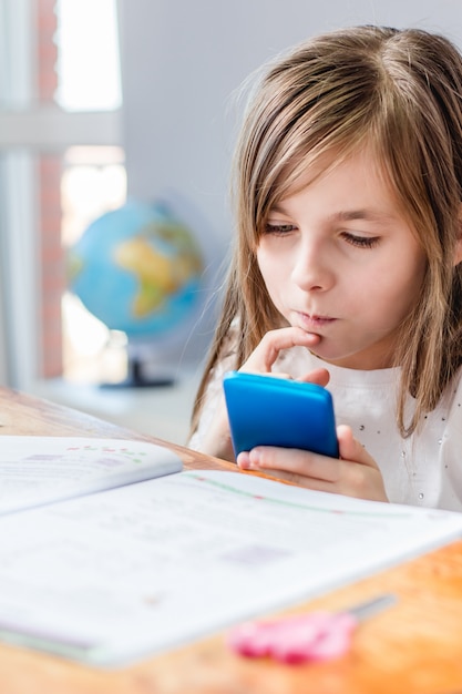 Young girl doing homework and using smartphone